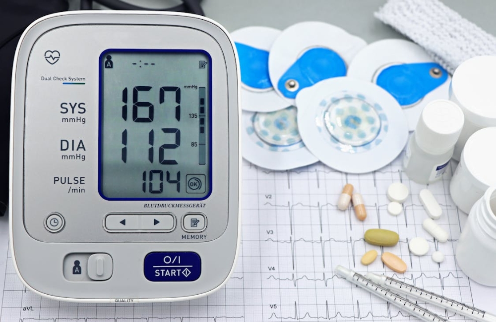 Close-up view of an electronic automatic blood pressure monitor reading next to a doctor charting patient metrics