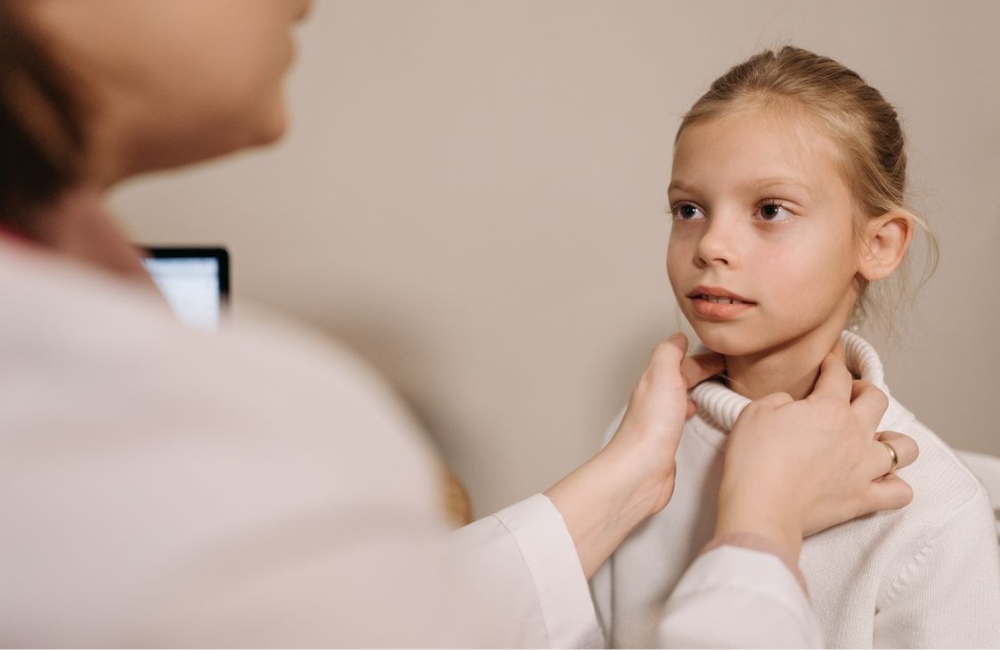 A female physician gently placing gloved hands on a patient's neck to check for thyroid nodules or swelling