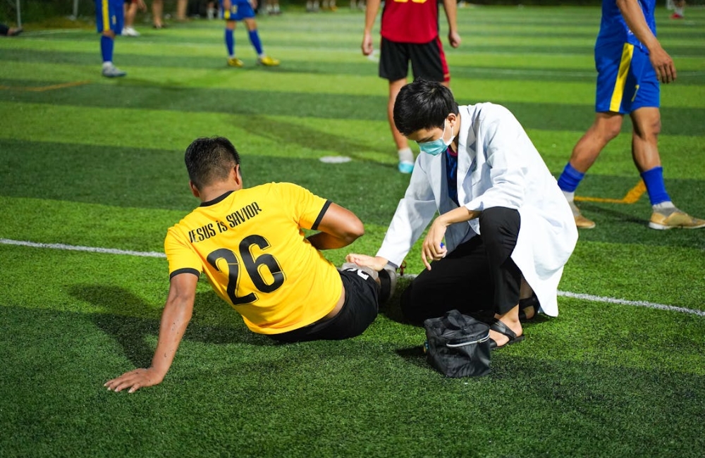 Orthopedic practitioner examining and bandaging a patient's injured knee joint in a modern clinical room