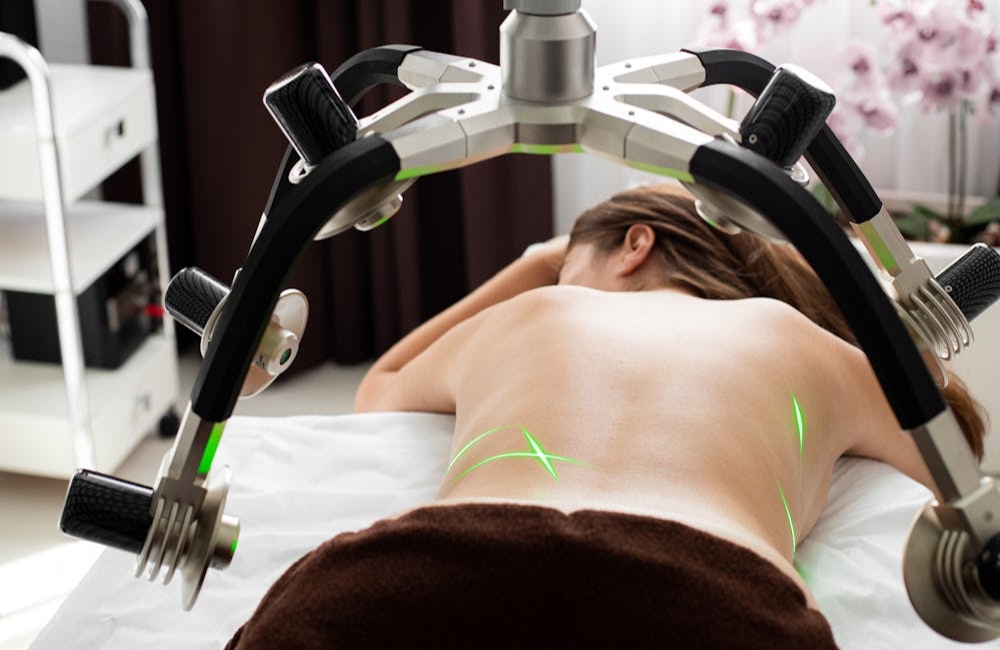 Physiotherapist applying advanced electromagnetic targeted machine therapy to a female patient's lower back pain zone